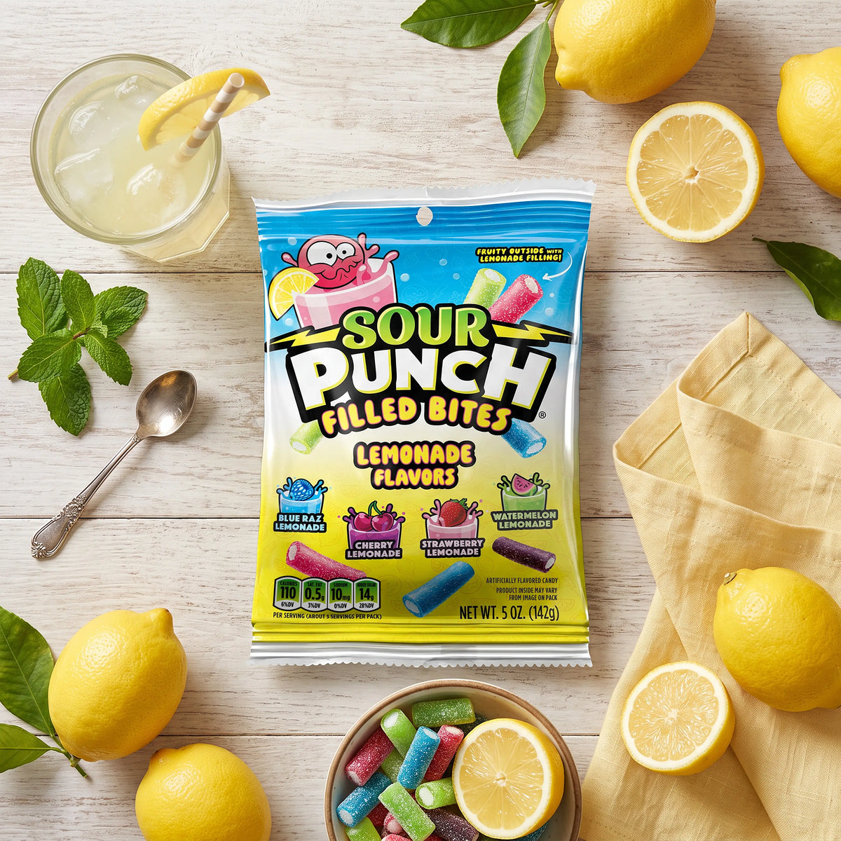 Sour Punch Lemonade Filled Bites 5oz Bag on a table with lemons, candy bites, and fresh lemonade