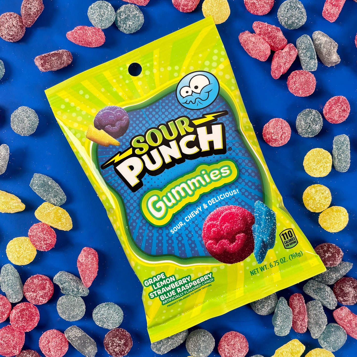Sour Punch Gummies on a blue background with raw candies surrounding the bag